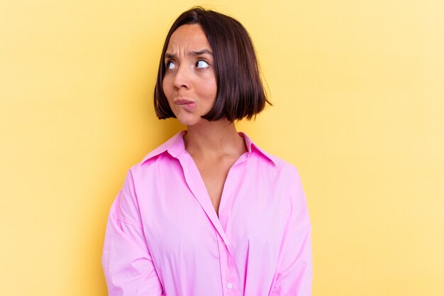 Mulher jovem de raça mista isolada em fundo amarelo confusa, sente-se em dúvida e insegura.