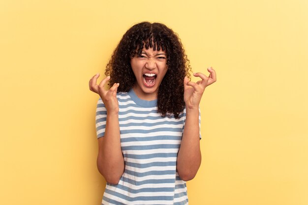 Mulher jovem de raça mista isolada em fundo amarelo, gritando de raiva.