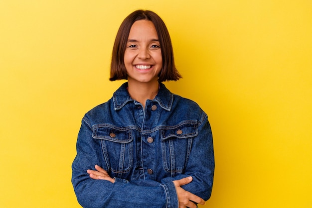 Mulher jovem de raça mista isolada em fundo amarelo que se sente confiante, cruzando os braços com determinação.