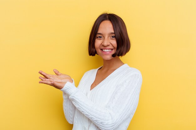 Mulher jovem de raça mista isolada em fundo amarelo, segurando um espaço de cópia na palma da mão.