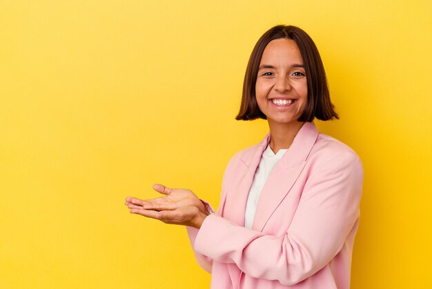 Mulher jovem de raça mista isolada em fundo amarelo, segurando um espaço de cópia na palma da mão.