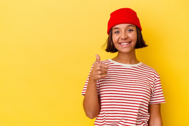 Mulher jovem de raça mista isolada em fundo amarelo sorrindo e levantando o polegar