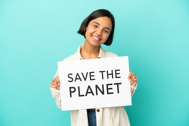 Mulher jovem de raça mista isolada em fundo azul segurando um cartaz com o texto Salve o Planeta com uma expressão feliz