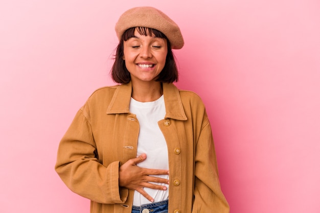 Mulher jovem de raça mista isolada em fundo rosa toca a barriga, sorri suavemente, conceito de comer e satisfação.