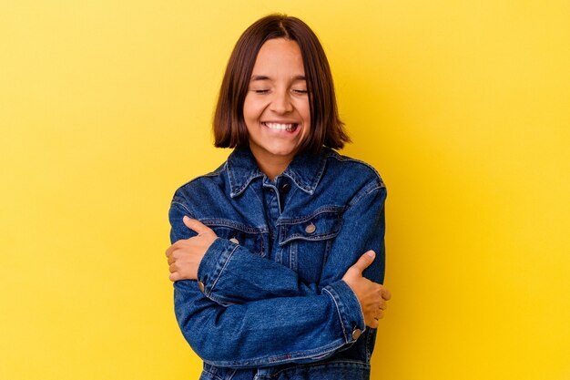 Mulher jovem de raça mista isolada em um fundo amarelo abraços, sorrindo despreocupada e feliz.