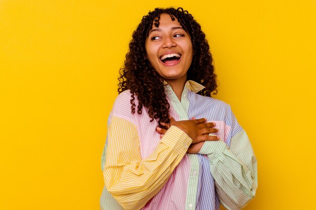 Mulher jovem de raça mista isolada na parede amarela rindo mantendo as mãos no coração, o conceito de felicidade.