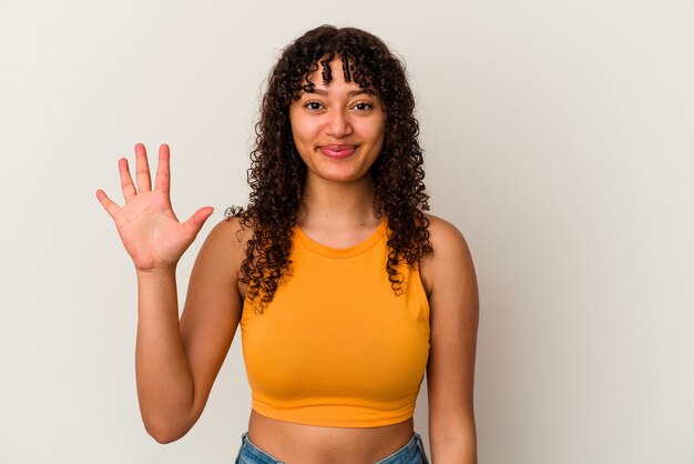 Mulher jovem de raça mista isolada na parede branca, sorrindo alegre mostrando o número cinco com os dedos.