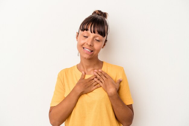 Mulher jovem de raça mista isolada no fundo branco tem uma expressão amigável, pressionando a palma da mão no peito. Conceito de amor.