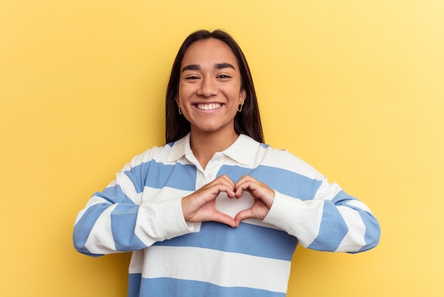 Mulher jovem de raça mista isolada sorrindo e mostrando uma forma de coração com as mãos.