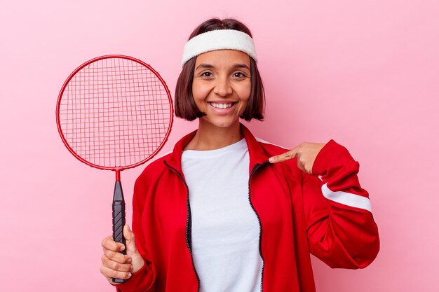 Mulher jovem de raça mista jogando badminton isolada na parede rosa pessoa apontando com a mão para um espaço de cópia de camisa, orgulhosa e confiante