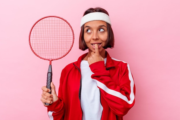 Mulher jovem de raça mista jogando badminton isolado na parede rosa relaxada pensando em algo olhando para um espaço de cópia.