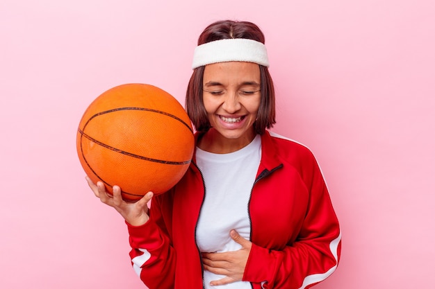 Mulher jovem de raça mista jogando basquete isolado no fundo rosa, rindo e se divertindo.