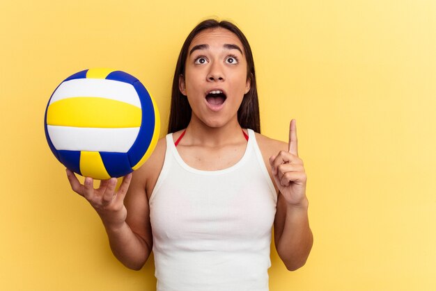 Mulher jovem de raça mista jogando vôlei na praia isolada em um fundo amarelo apontando de cabeça para baixo com a boca aberta.