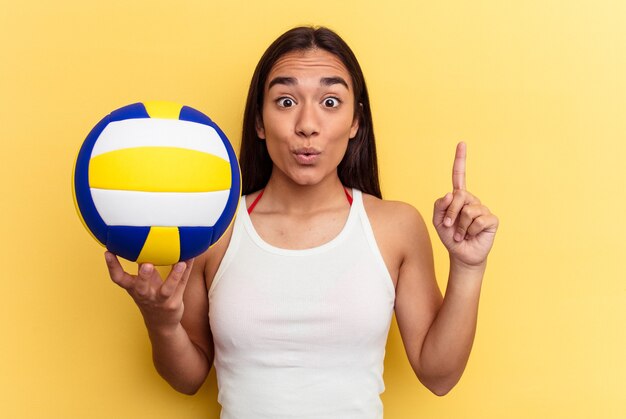 Mulher jovem de raça mista jogando vôlei na praia isolada no fundo amarelo, tendo uma ótima ideia, o conceito de criatividade.