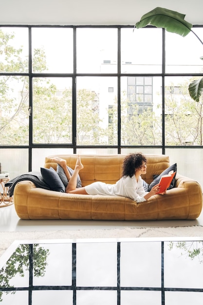 Mulher jovem de raça mista lendo um livro na sala de estar de casa Copie o espaço Imagem vertical Conceito de estilo de vida