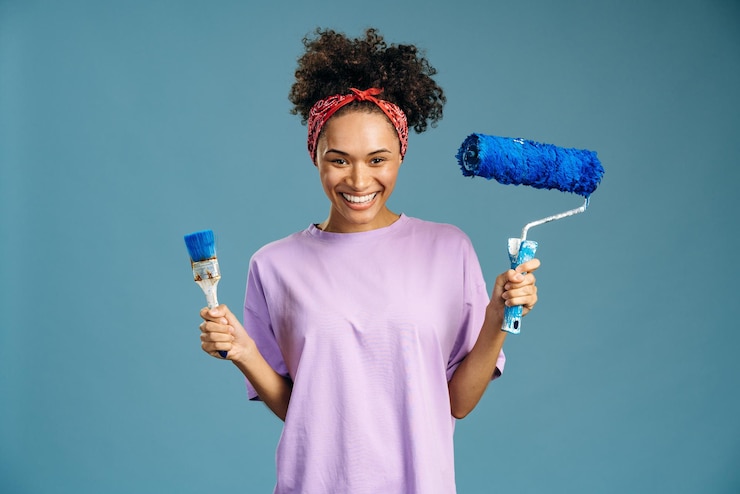 Foto mulher jovem de raça mista satisfeita, aproveitando o tempo de renovação em casa, segurando o pincel e o rolo. conceito de reparo e remodelação