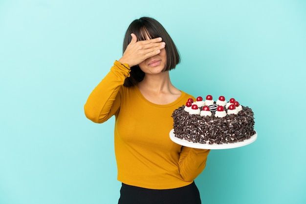 Mulher jovem de raça mista segurando o bolo de aniversário, cobrindo os olhos pelas mãos. Não quero ver nada