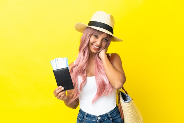 Mulher jovem de raça mista segurando passaporte e bolsa de praia isolada em um fundo amarelo rindo