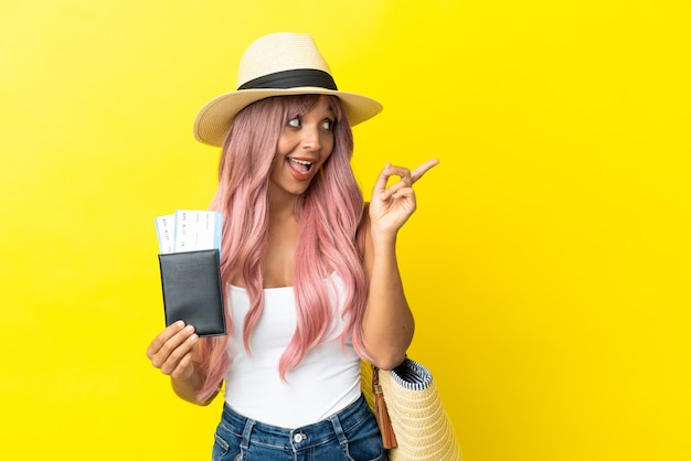 Mulher jovem de raça mista segurando passaporte e bolsa de praia isolados em um fundo amarelo com a intenção de descobrir a solução enquanto levanta um dedo