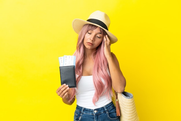 Mulher jovem de raça mista segurando passaporte e bolsa de praia isolados em um fundo amarelo com dor de cabeça