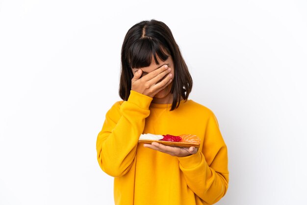 Mulher jovem de raça mista segurando sashimi isolado no fundo branco com expressão cansada e doente