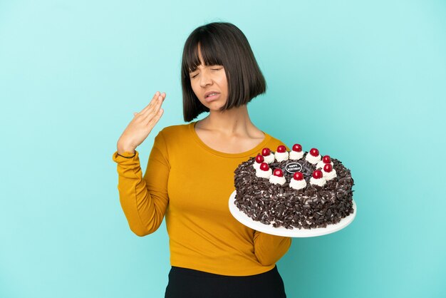 Mulher jovem de raça mista segurando um bolo de aniversário com uma expressão cansada e doente