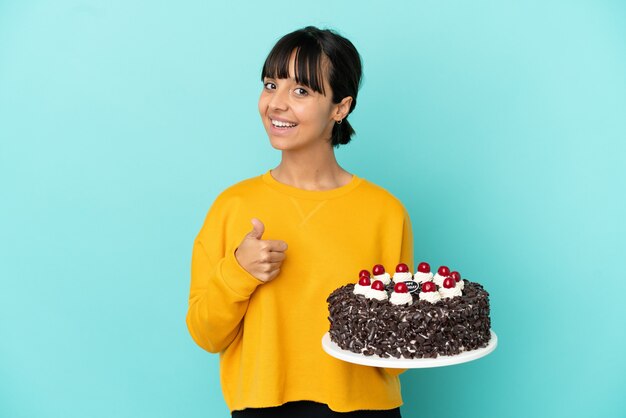 Mulher jovem de raça mista segurando um bolo de aniversário e fazendo um gesto de polegar para cima