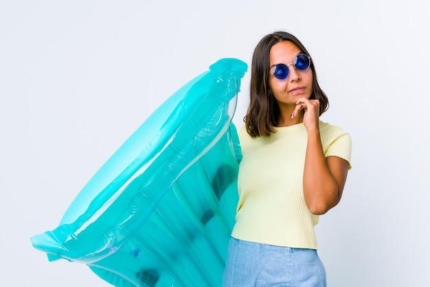 Mulher jovem de raça mista segurando um colchão de ar relaxada pensando em algo olhando para um espaço de cópia.