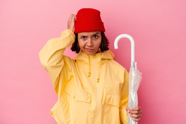 Mulher jovem de raça mista segurando um guarda-chuva isolado em um fundo rosa sendo chocada, ela se lembrou de uma reunião importante.