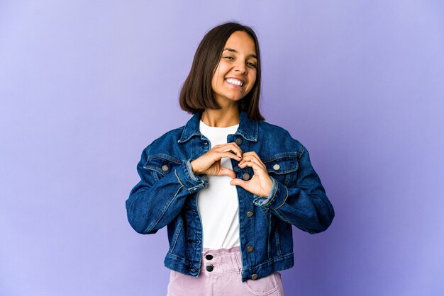 Mulher jovem de raça mista sorrindo e mostrando uma forma de coração com as mãos.