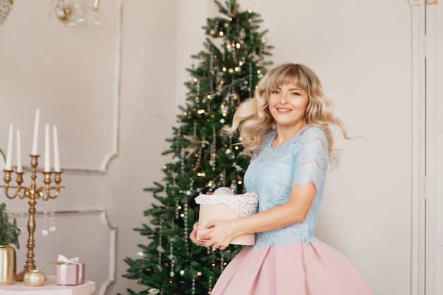 Mulher jovem decora a árvore de Natal com brinquedos de Natal. Interior clássico em branco e dourado