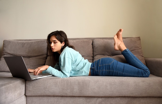 Mulher jovem deitada no sofá e usando o laptop em casa