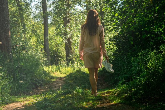 Mulher jovem, depois de nadar no rio, caminha descalça ao longo da estrada da floresta