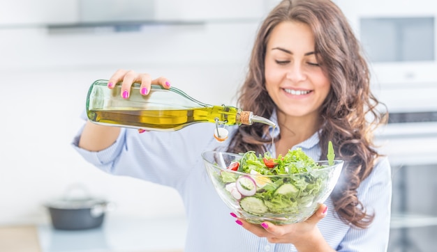 Mulher jovem derramando azeite na salada. Conceito de comer estilo de vida saudável.