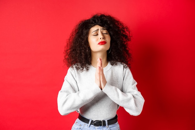 Mulher jovem desesperada suplicando a Deus, fazendo desejos e suplicando de mãos dadas em orar com os olhos fechados ...