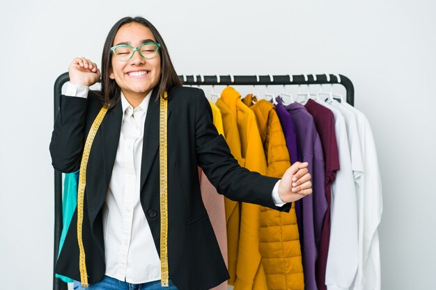 Mulher jovem designer asiática isolada na parede branca, dançando e se divertindo.