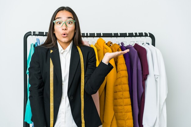 Mulher jovem designer asiática isolada na parede branca impressionada, segurando o espaço da cópia na palma da mão.