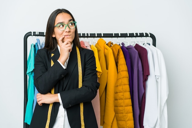 Mulher jovem designer asiática isolada no branco, olhando de soslaio com expressão duvidosa e cética.