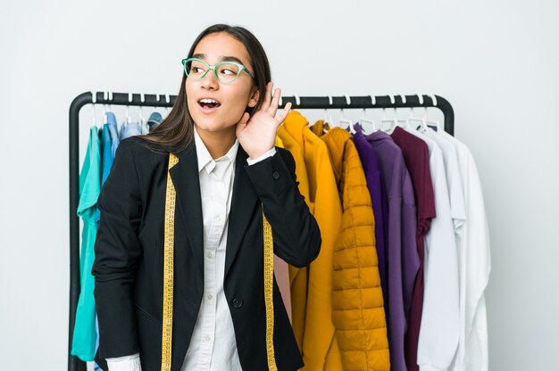 Mulher jovem designer asiática isolada no branco, tentando ouvir uma fofoca.