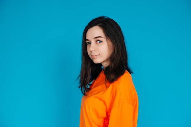 Mulher jovem deslumbrante em poses de roupa laranja da moda para retrato isolado em fundo azul Modelo adorável com um olhar cativante e aparência deslumbrante