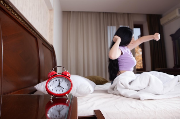 Foto mulher jovem dormindo e segurando despertador na cama