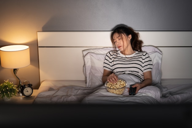 Foto mulher jovem dormindo enquanto assiste tv em uma cama à noite