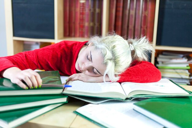 Foto mulher jovem dormindo na secretária enquanto estuda na biblioteca