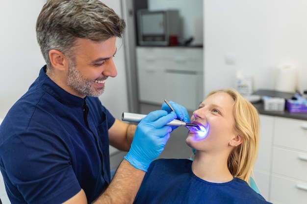 Mulher jovem durante o procedimento de secagem de preenchimento dentário com luz ultravioleta de cura na clínica odontológica