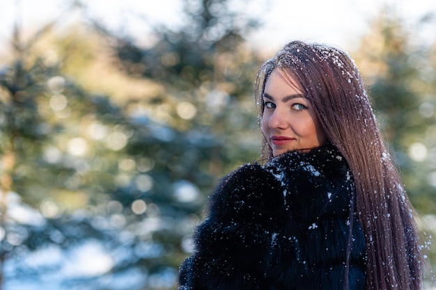 Mulher jovem e alegre com um casaco de pele quente, curtindo um dia de inverno no bosque nevado