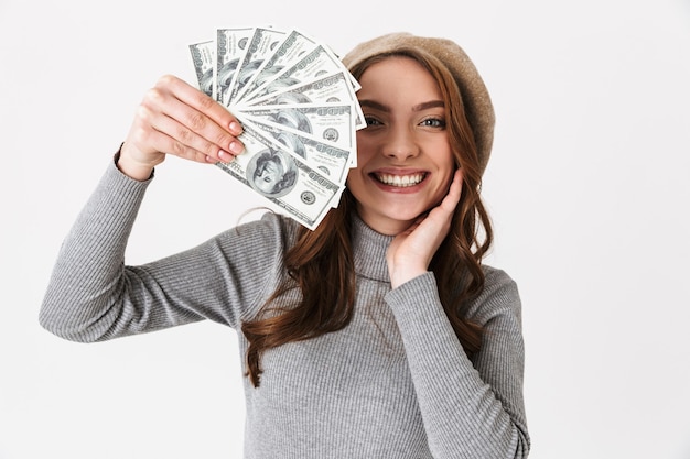 Mulher jovem e alegre em pé, isolada sobre uma parede branca, mostrando notas de dinheiro