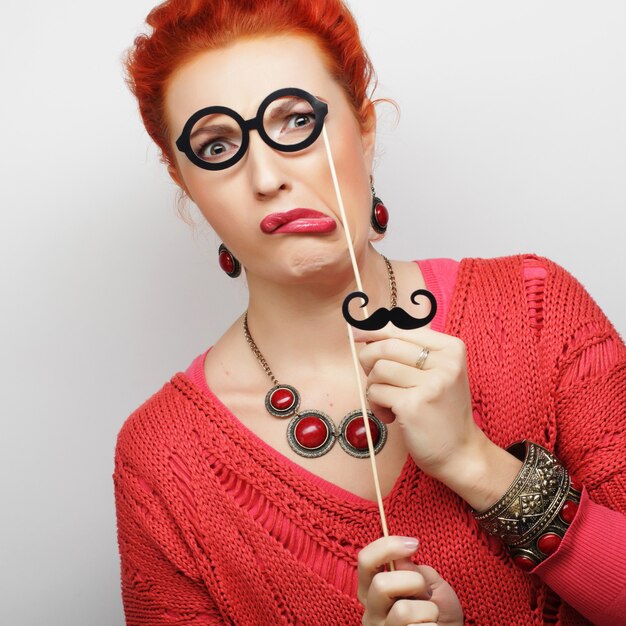 Mulher jovem e atraente brincalhão segurando bigode e óculos no palito. Pronto para a festa.