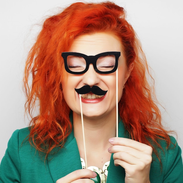 Mulher jovem e atraente brincalhão segurando bigode e óculos no palito. Pronto para a festa.