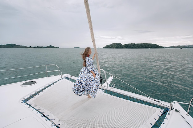 Mulher jovem e atraente caucasiana em vestido colorido em pé no iate, menina nadar oceano água do mar férias férias de verão. Phuket. Tailândia. Foto com ruído