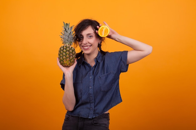 Mulher jovem e atraente caucasiana segurando um abacaxi na mão sobre um fundo amarelo no estúdio. mulher com deliciosas frutas exóticas.
